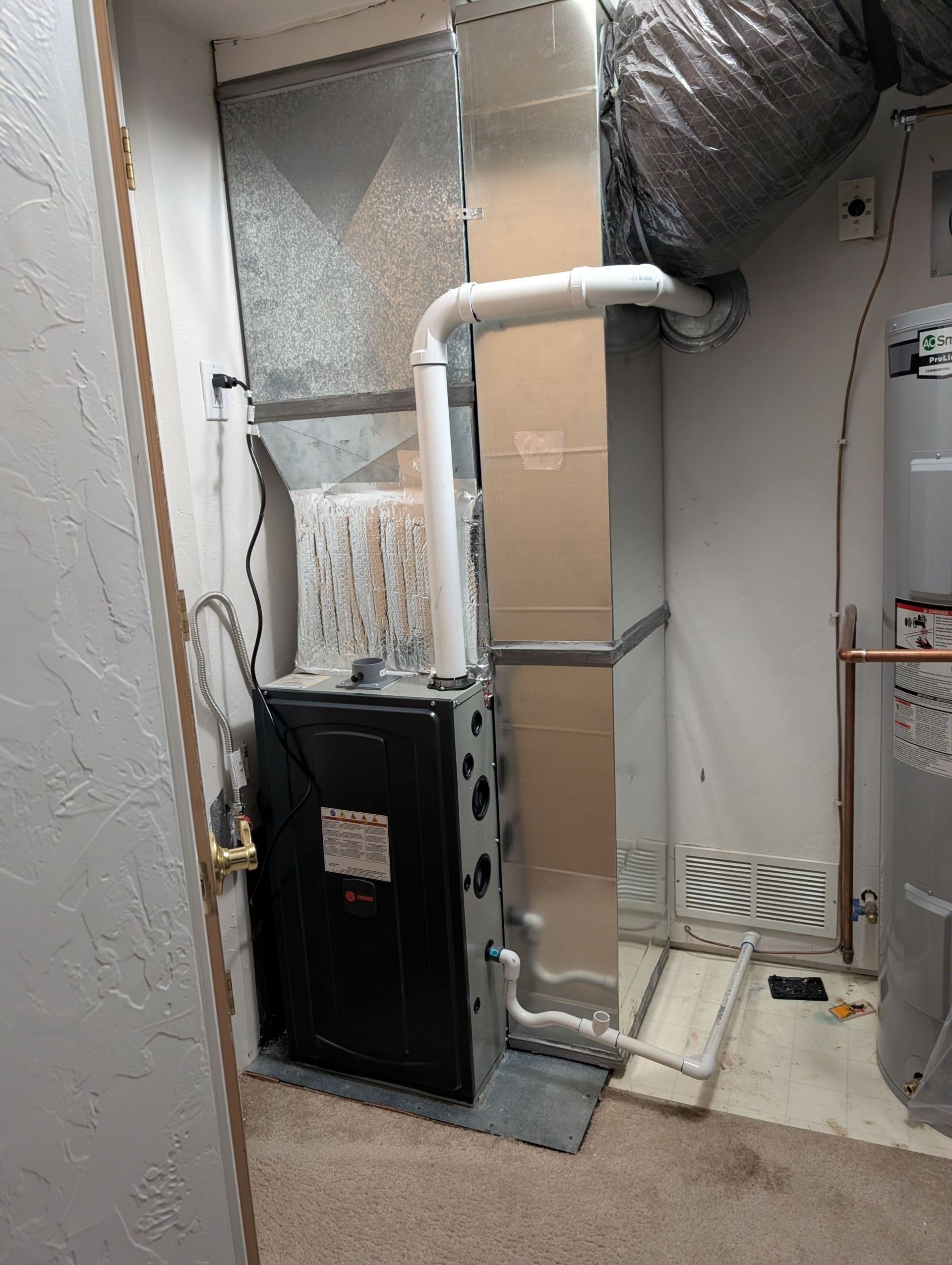 Furnace in a utility room. Rectangular metal unit with connected ductwork. Beige walls and carpet.