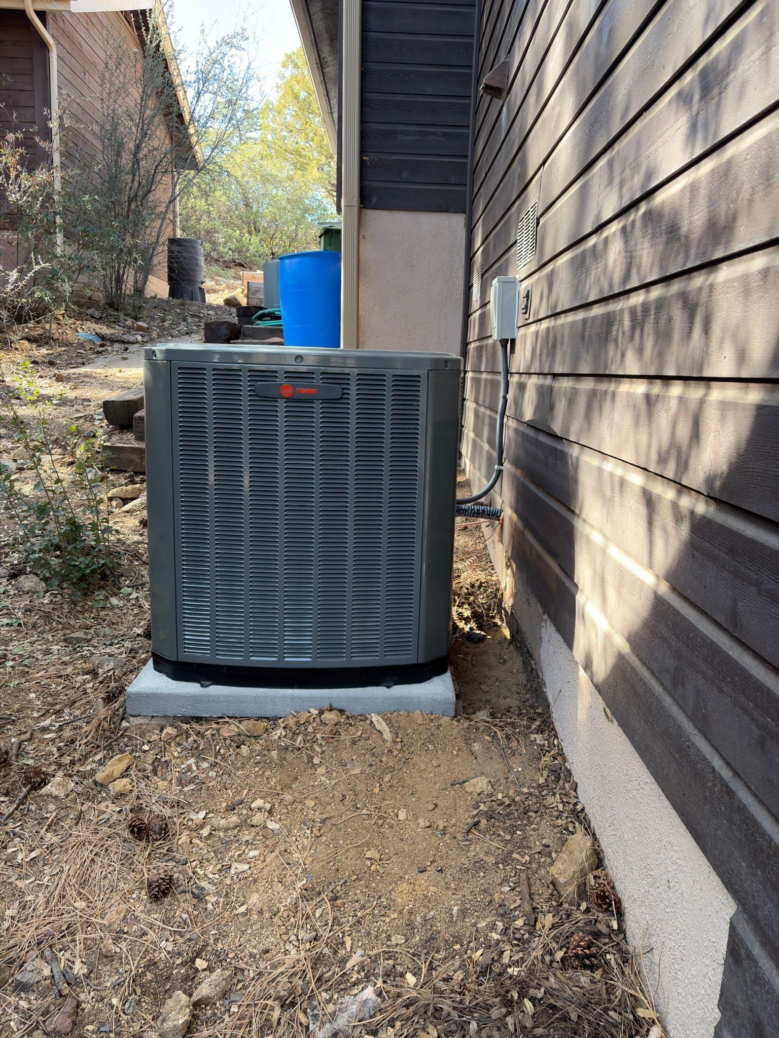 Gray air conditioning unit on a concrete pad next to a wood-sided building.