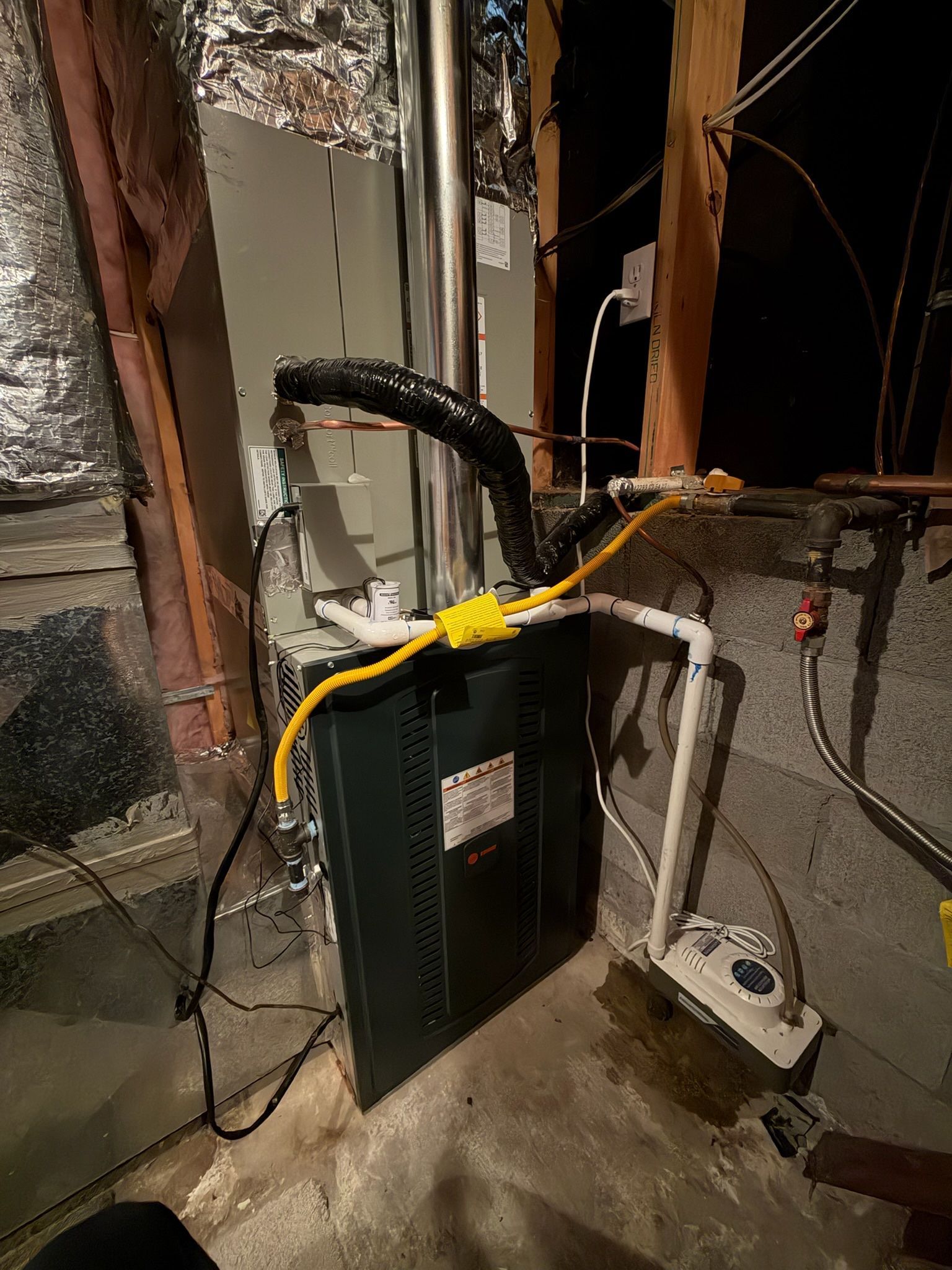 Furnace system with metal flue, black insulation, and yellow electrical wire in a utility room.