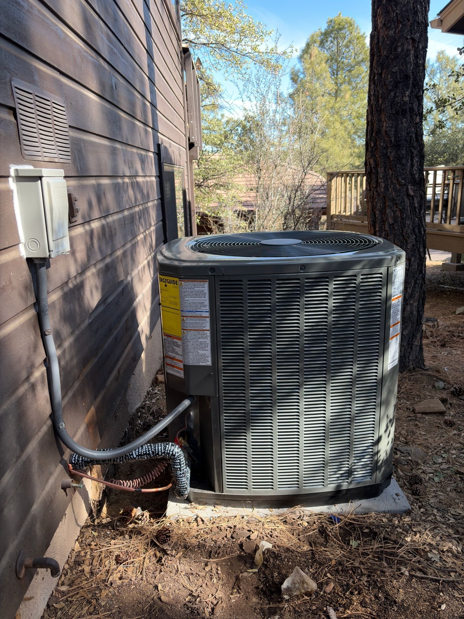 Outdoor AC unit next to a wooden building, with power and refrigerant lines attached.