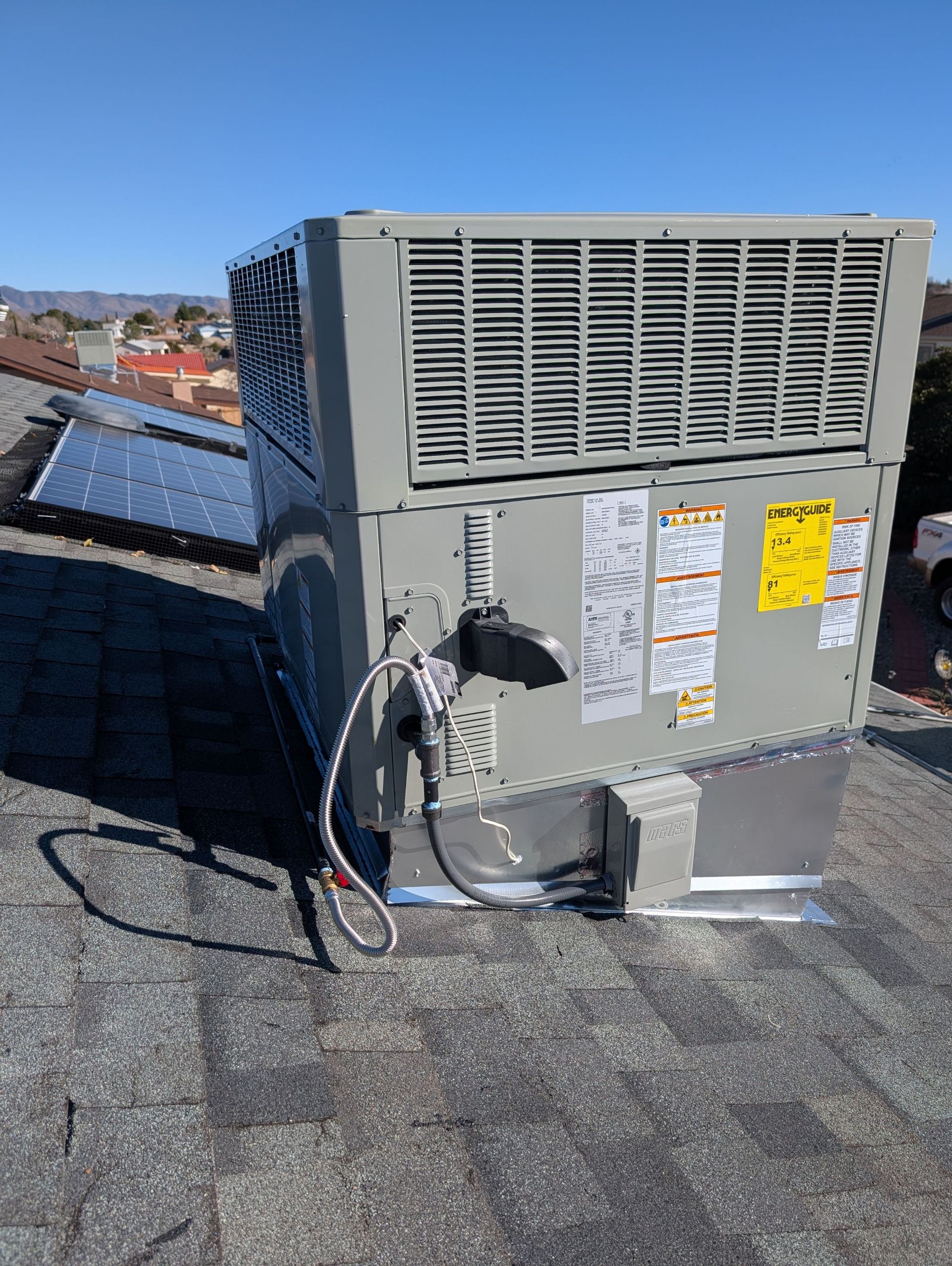 HVAC unit on a rooftop, gray and silver with warning labels, solar panels visible nearby.
