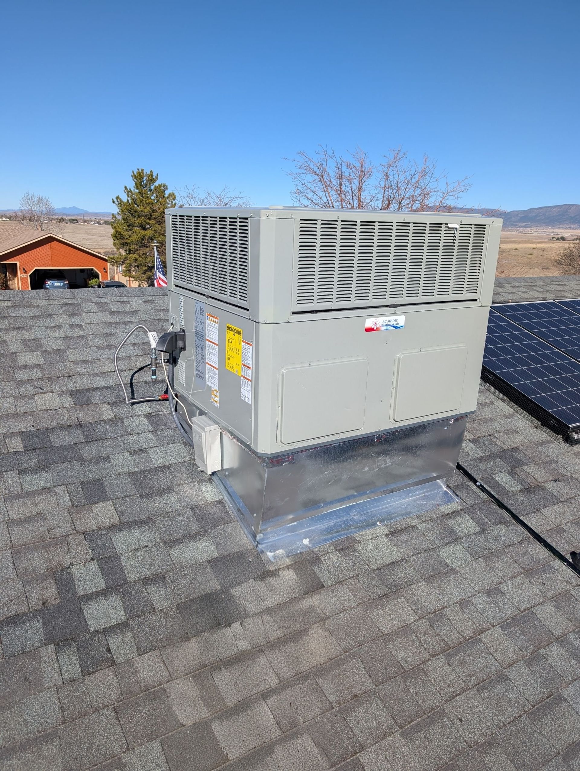 Rooftop HVAC unit on a shingled roof under a clear blue sky.