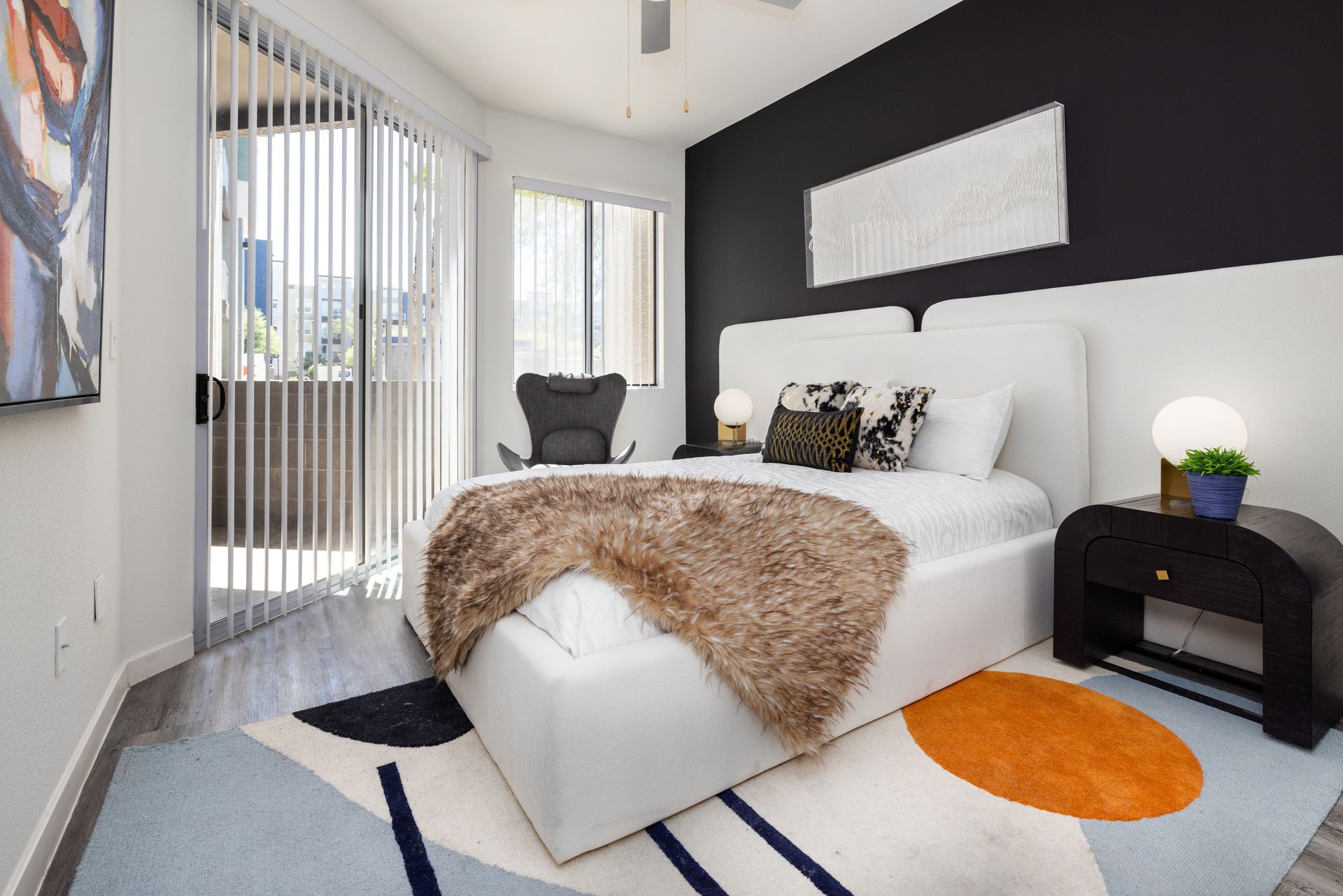 Bedroom with white bed, black accent wall, balcony, and colorful rug.