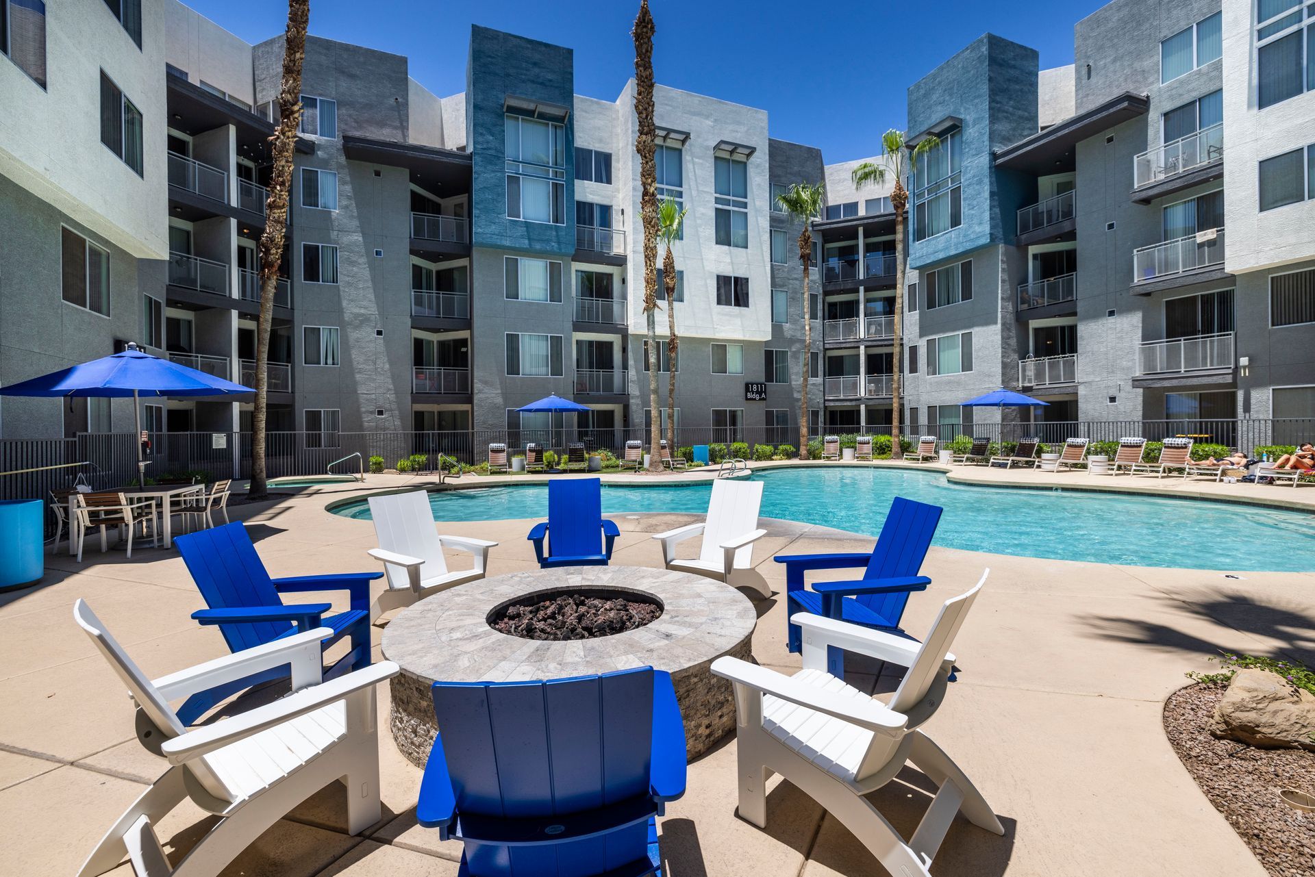 Apartment complex courtyard with pool, fire pit, and blue and white chairs.