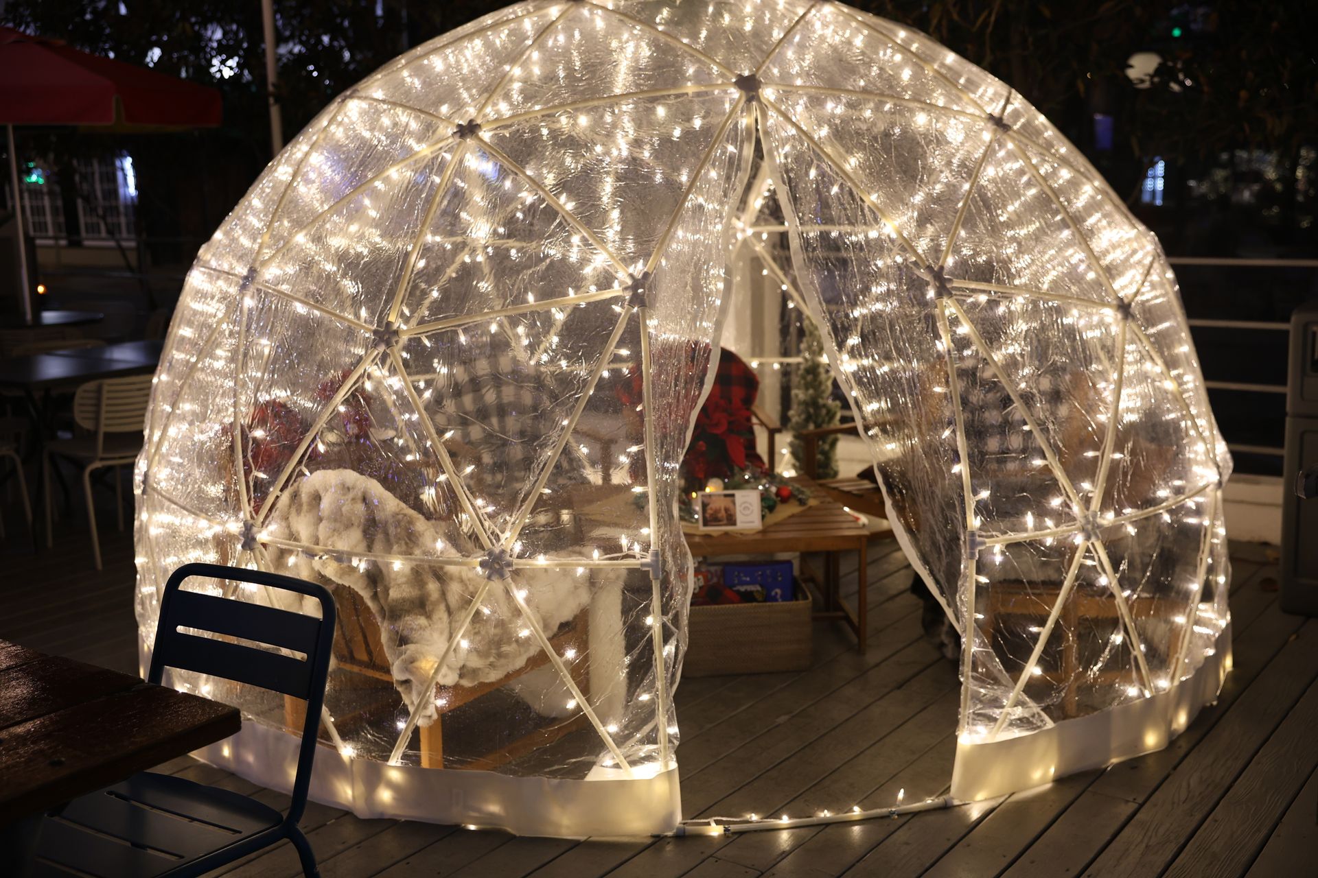 Igloo-shaped dining structure with string lights, table, chairs, on a deck, at night.