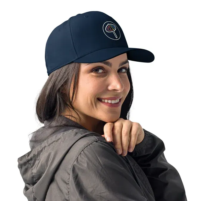 Woman wearing a navy blue cap with a logo, smiling, looking over her shoulder.