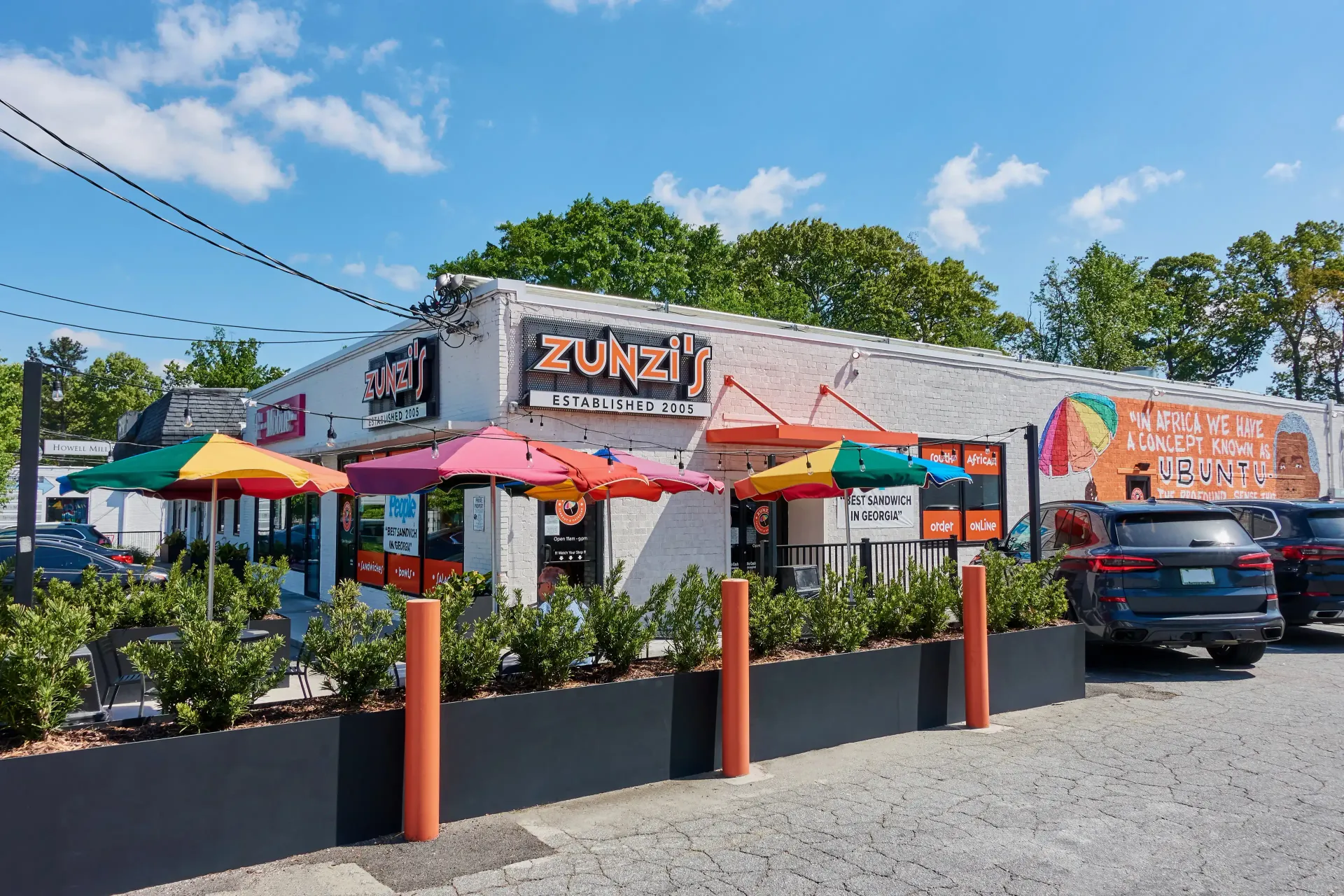 A restaurant with umbrellas and cars parked in front of it.