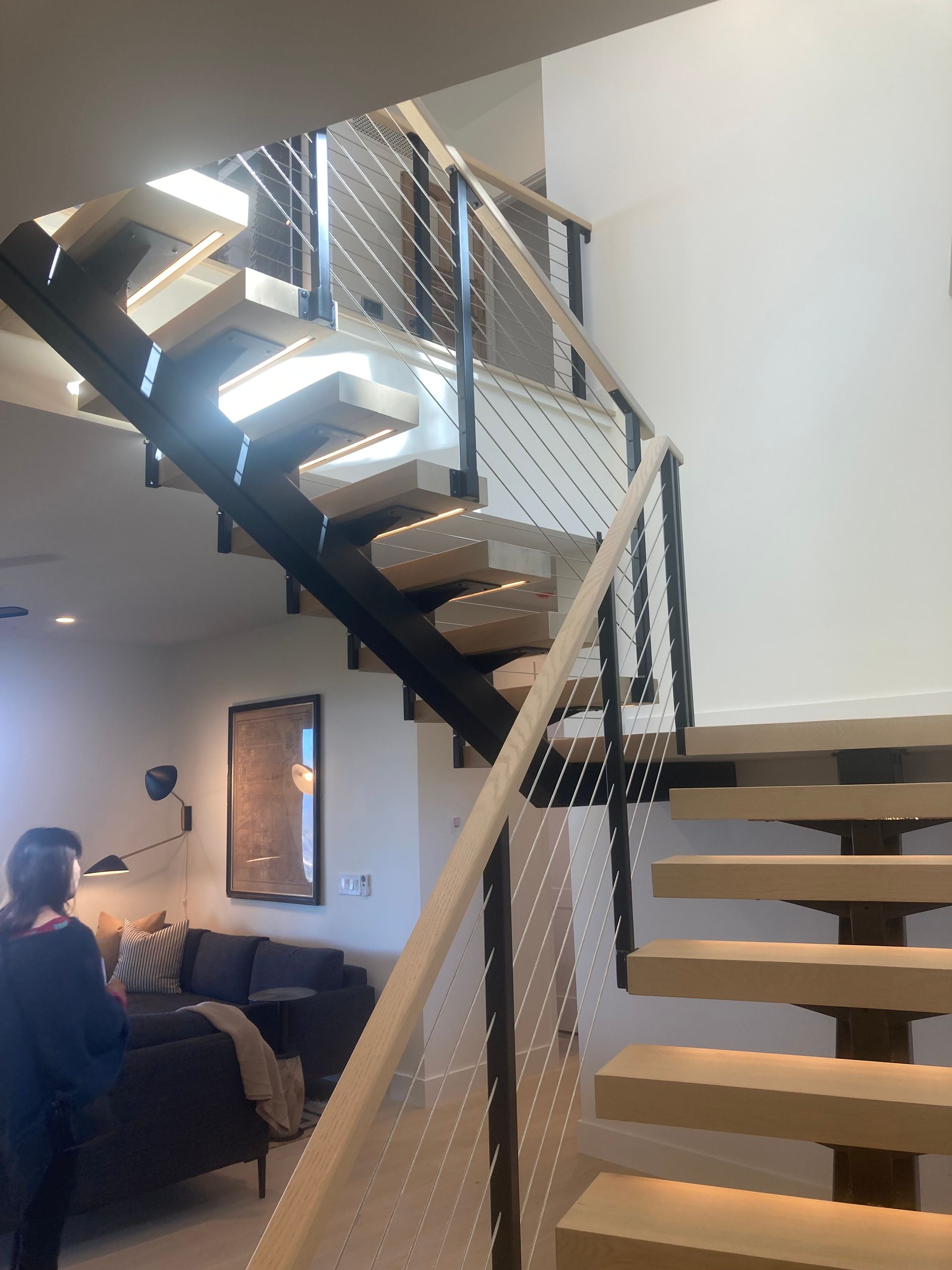 A woman is standing next to a staircase in a living room.
