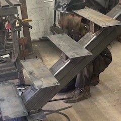 A man is working on a metal staircase in a workshop.