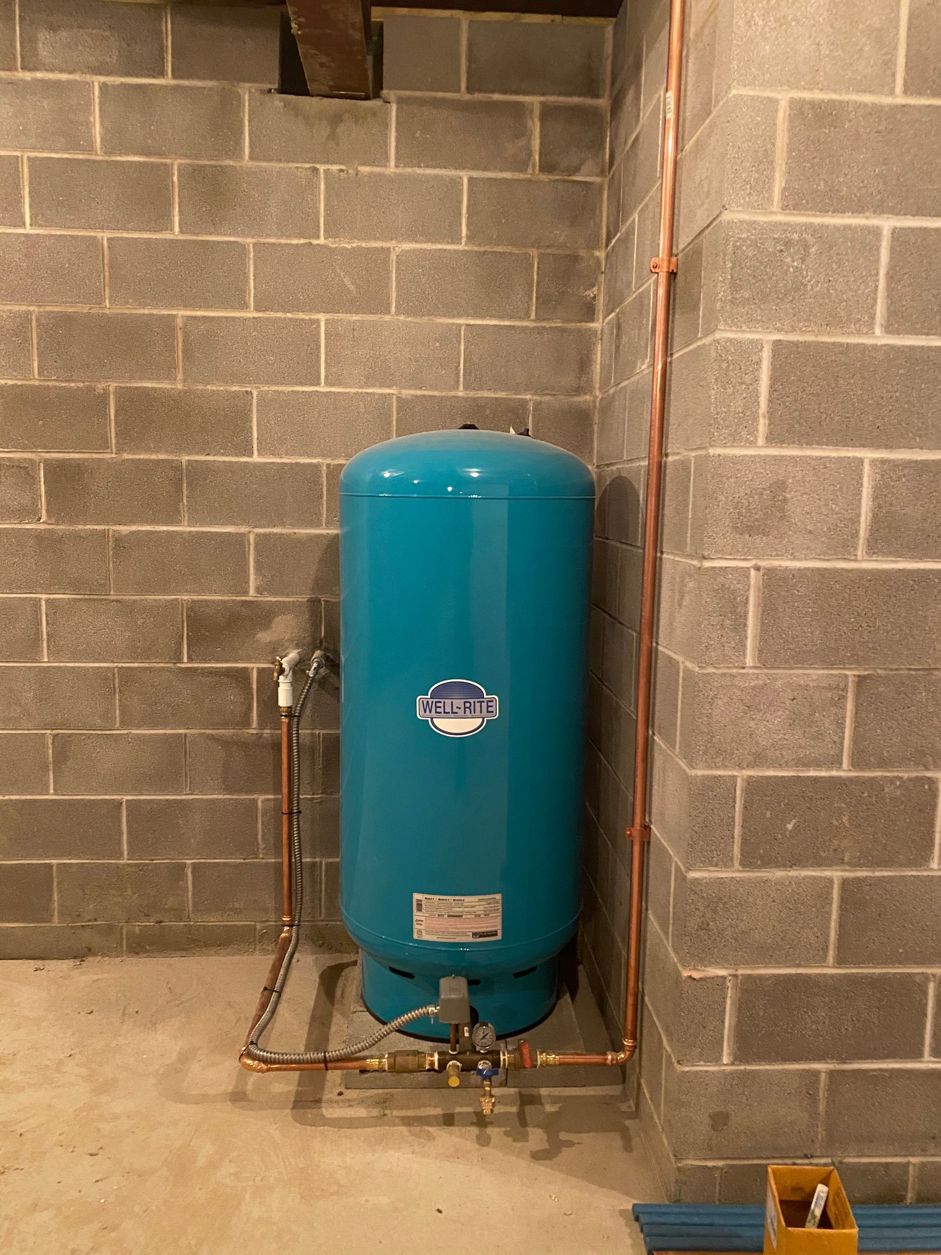 Blue water pressure tank in a corner of a cinder block room, copper pipes connected.