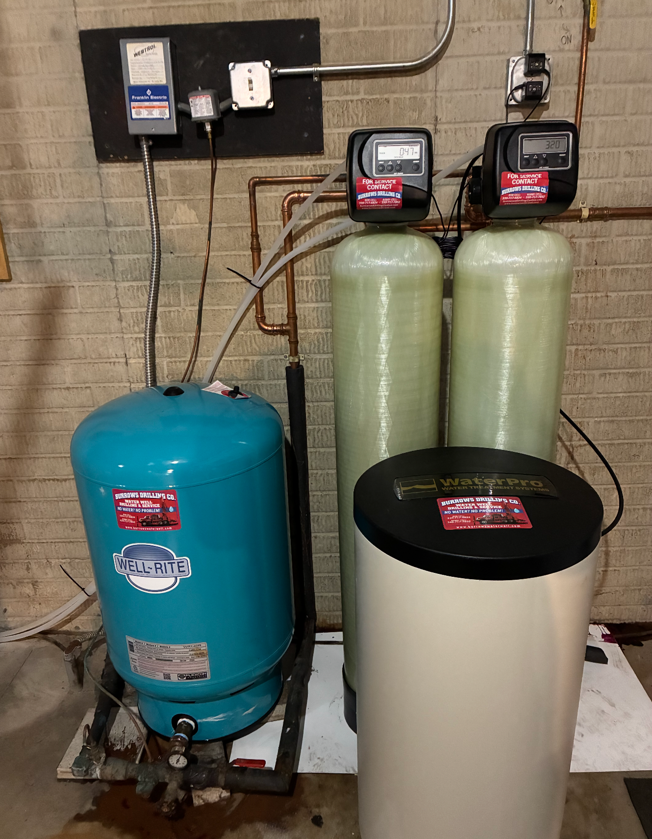 Water treatment system in a basement. Includes a pressure tank, two tall green tanks, and a white salt tank.