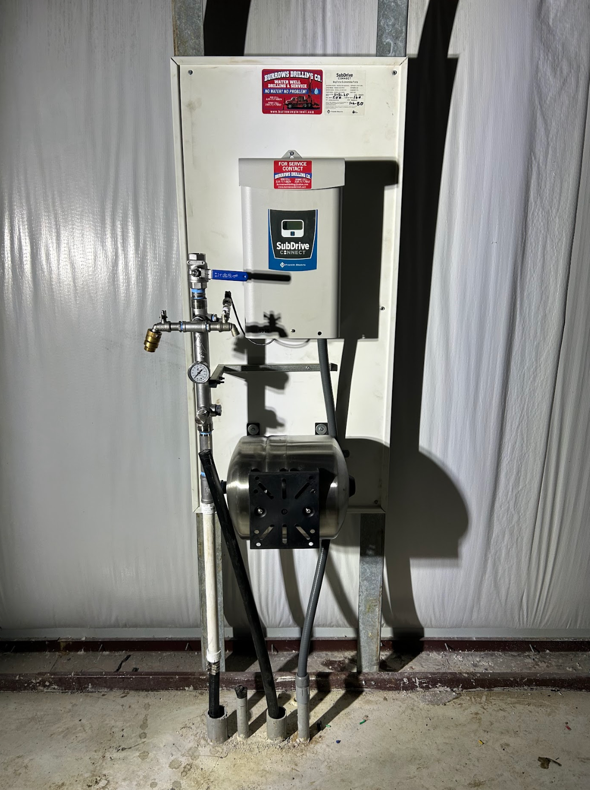 Wall-mounted water station with faucet, soap dispenser, and eyewash on a white backing panel, inside a room.