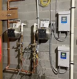 Pipes and pumps attached to a gray concrete block wall, with two white boxes labeled