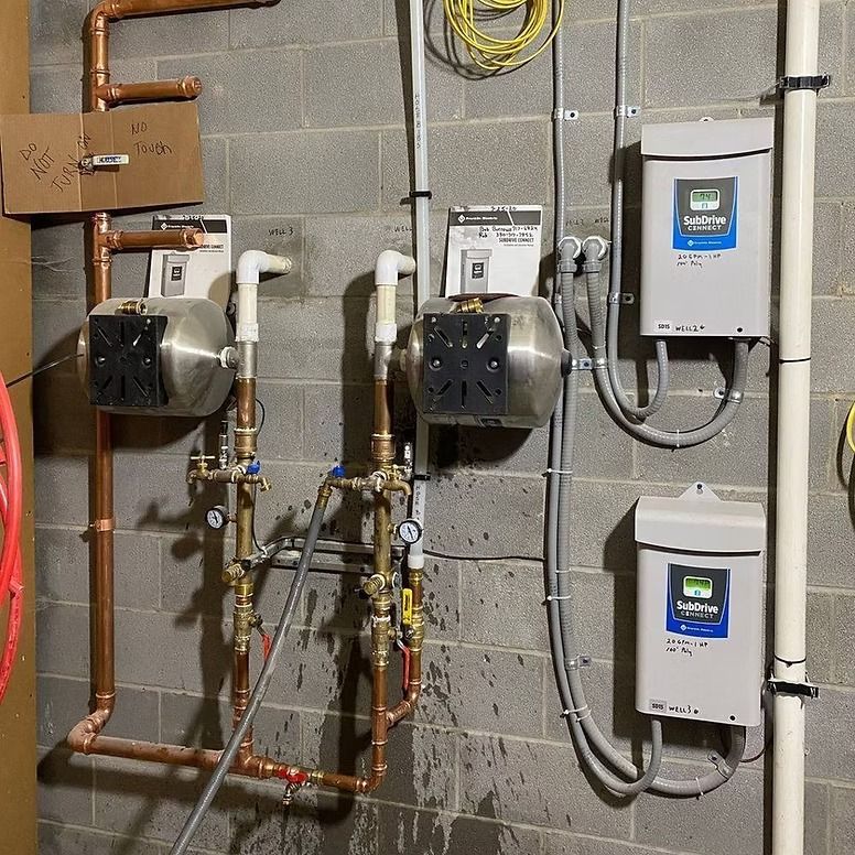 Water pump system with copper piping, gray concrete wall, and electrical components.