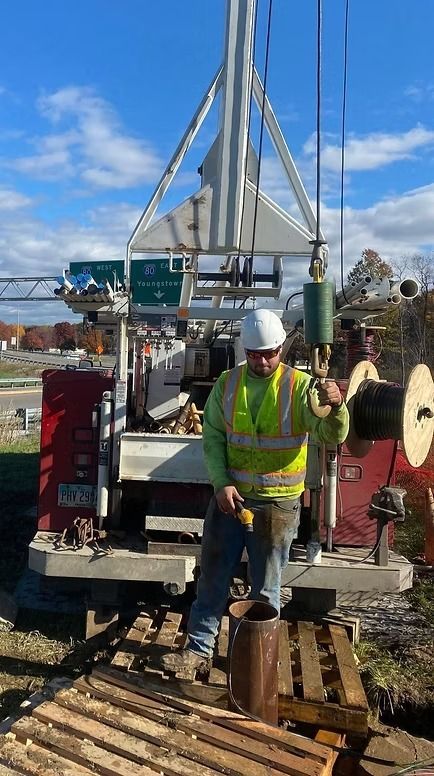 Construction worker operates drilling equipment outdoors on a sunny day.