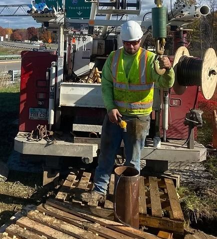 Construction worker in reflective vest operates drilling rig outdoors.