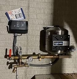 Water pump system mounted on a brick wall with gauges, pipes, and control panel.