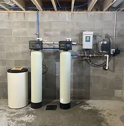 Two tall cylindrical tanks, a control panel, and plumbing against a concrete block wall.