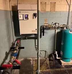 Electrical panel and water pump system in a basement setting. Pipes, tank, and various components visible.