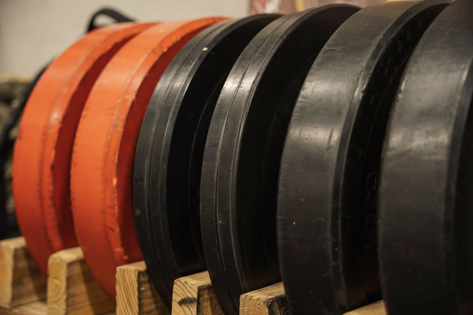 A row of red and black weight plates are lined up on a wooden rack.