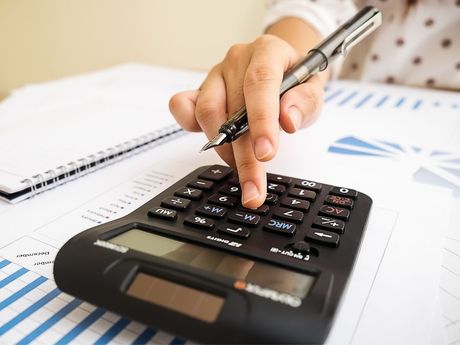 A person is using a calculator while holding a pen.