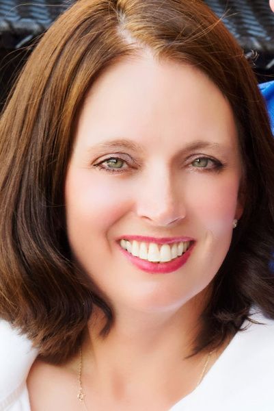 A woman with brown hair is smiling and wearing a white shirt.