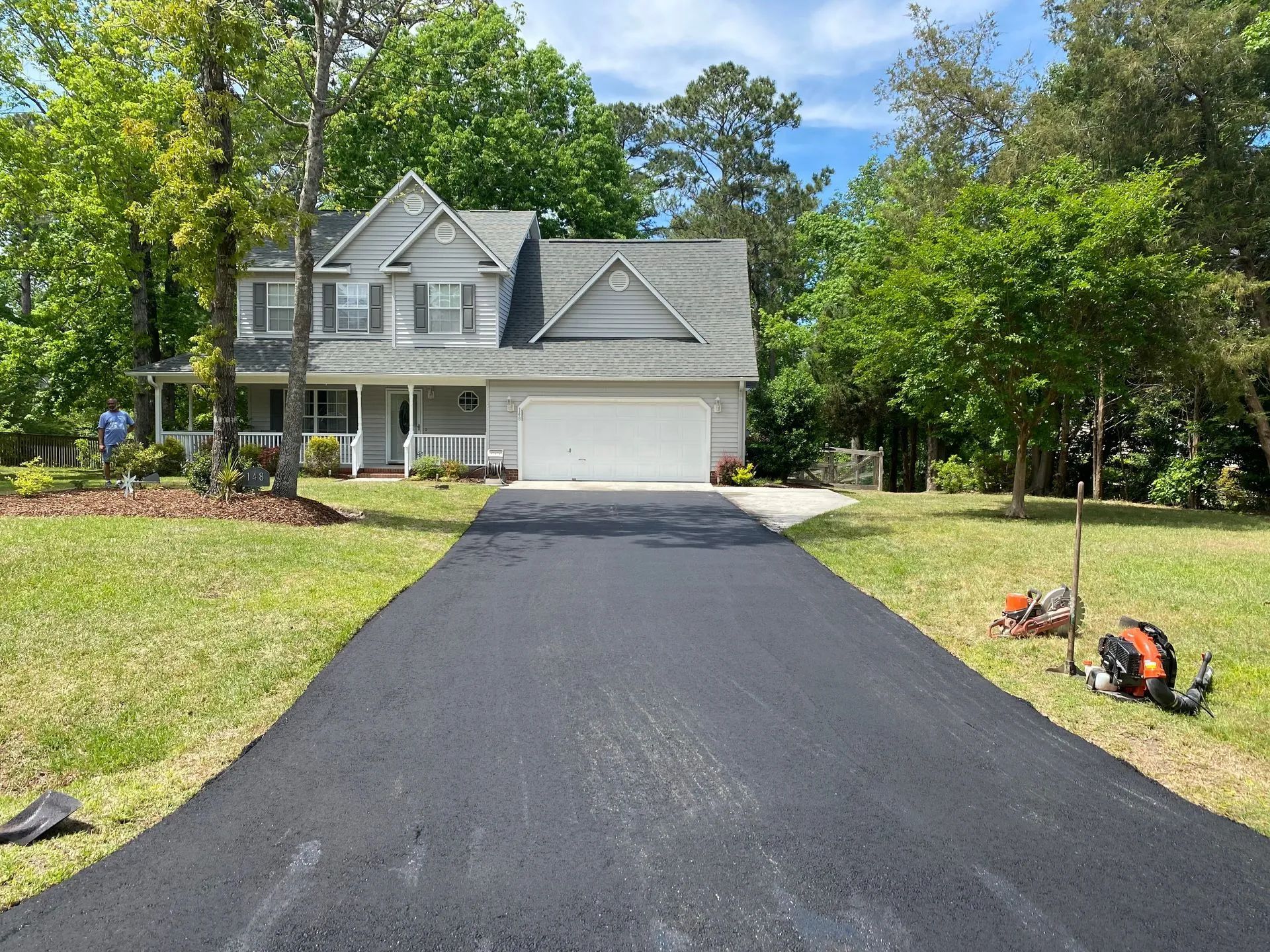 Gray house with a newly paved driveway. Landscaping and trees surround the house.