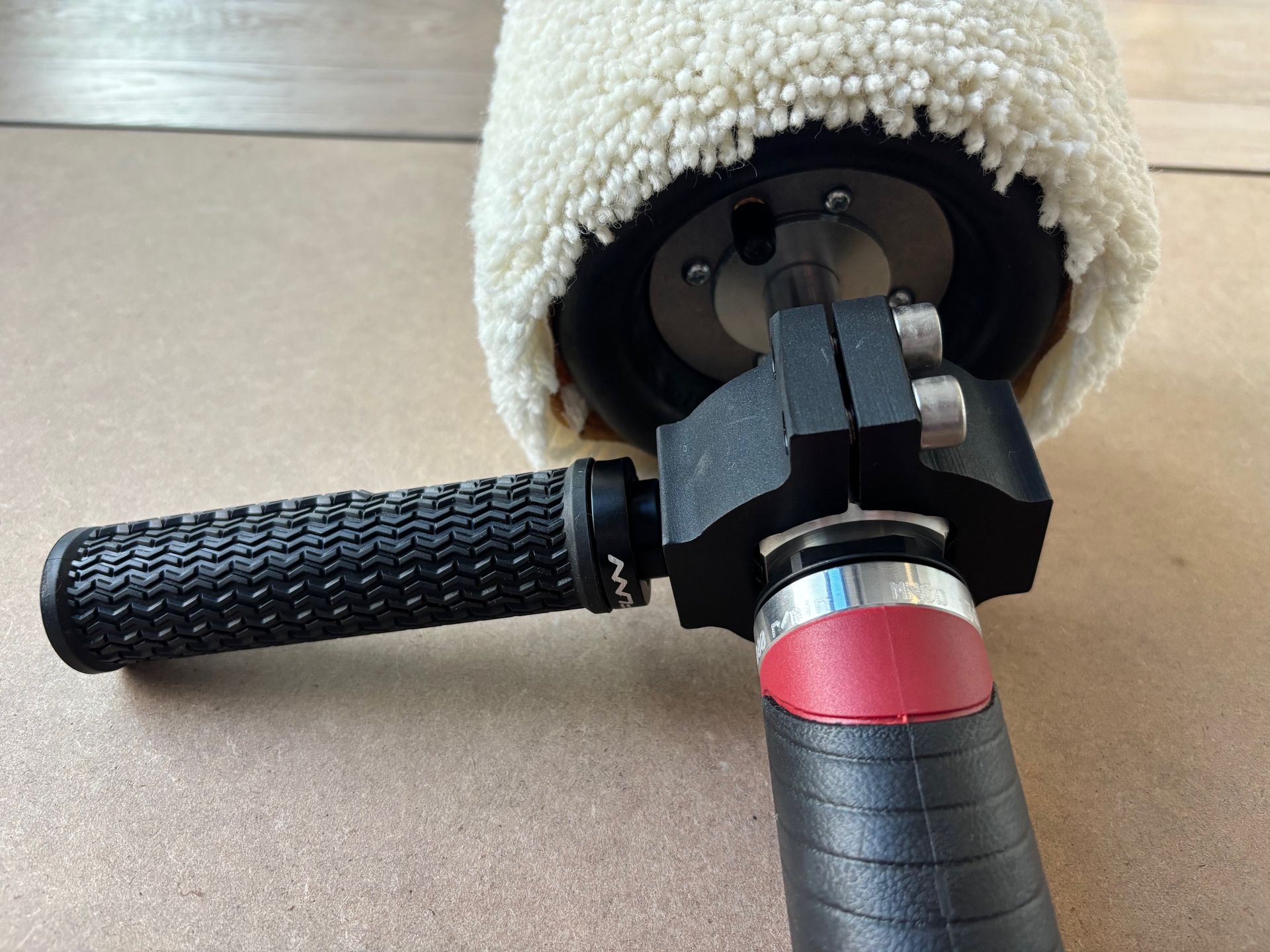Close-up of a black and red polishing tool with a sheepskin buffing pad and a black handle.