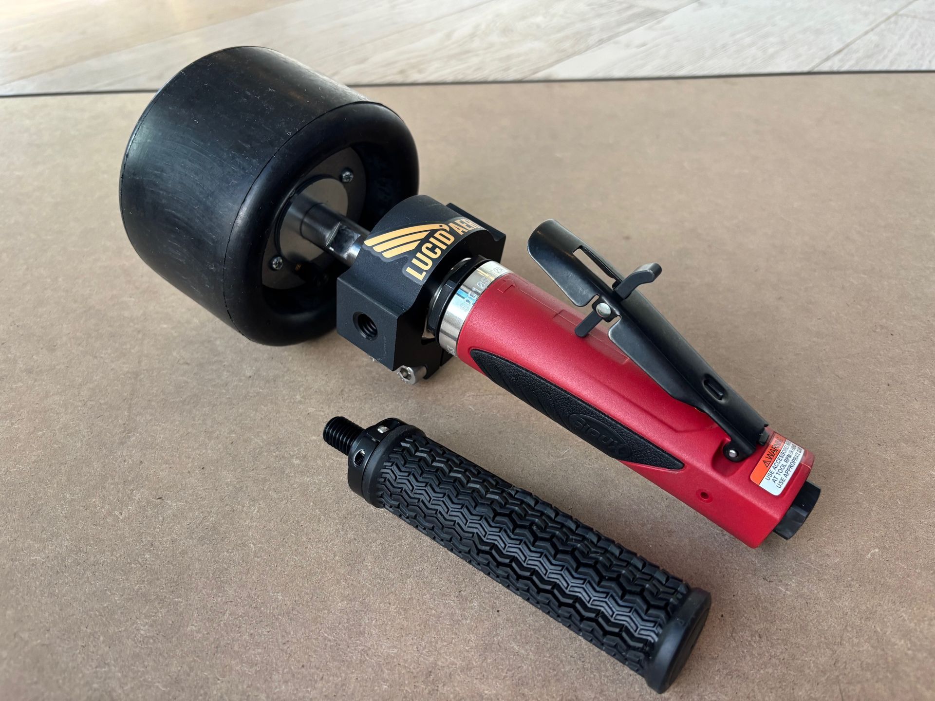 A tire inflator tool with a black tire attached, red handle, and black grip on a tan surface.