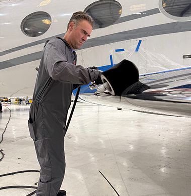 Person in gray jumpsuit polishing an airplane wing in a hangar.