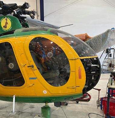 Yellow and green helicopter undergoing maintenance inside a hangar.