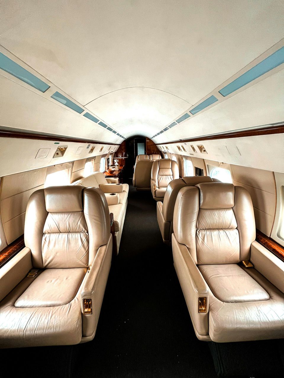 Interior of a private jet with beige leather seats and a dark carpet.