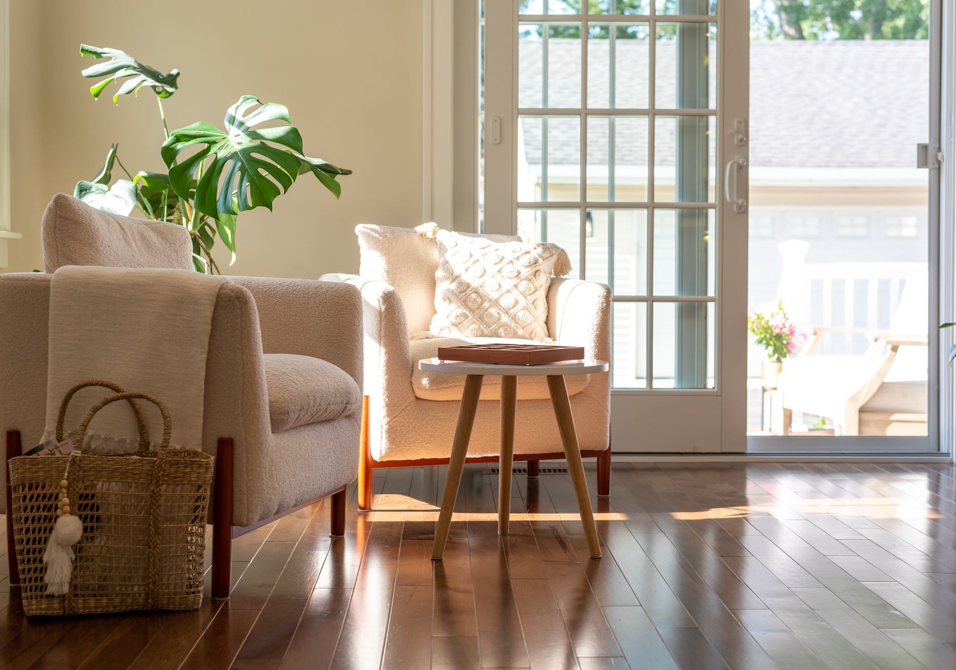 Sunlit living room with armchairs, a small table, a large plant, and a sliding glass door leading to a deck.