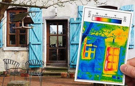Une personne tient une image thermique d'une maison aux volets bleus.