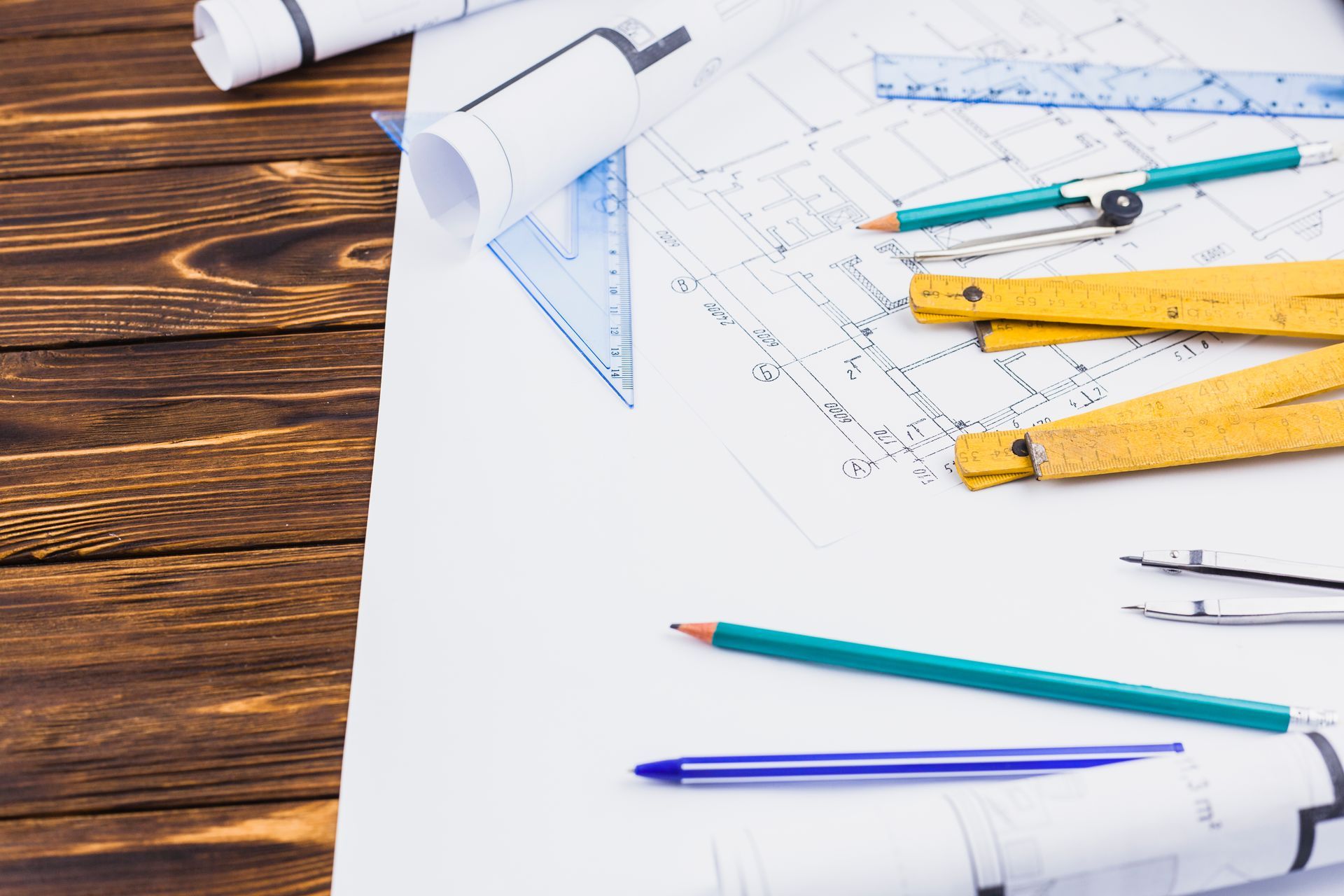 Une table en bois surmontée de plans, de crayons, de compas et de règles.