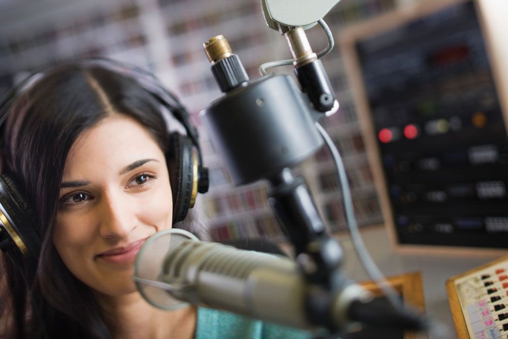 a woman wearing headphones is standing in front of a microphone in a radio station .
