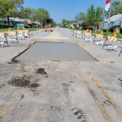 Road repair with freshly poured concrete, surrounded by traffic barriers on a sunny day.