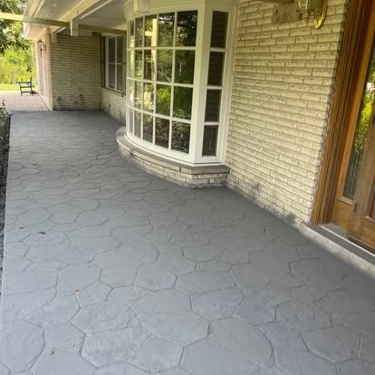 Gray concrete walkway with stone pattern, brick exterior, and a large bay window.