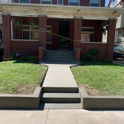 Brick house with porch, steps, and new concrete sidewalk. Green grass surrounds.