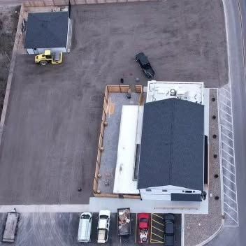 Aerial view of a building with a dark roof and a parking lot with several vehicles. Aerial view of a building with a dark roof and a parking lot with several vehicles.