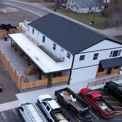 Two-story white building with a black roof and a wooden patio, cars parked in front.