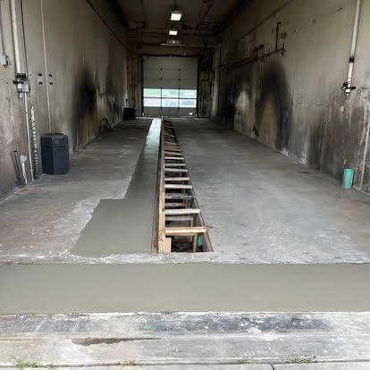 A repair bay with a partially covered inspection pit. Walls are dark, and a roll-up door is visible. A repair bay with a partially covered inspection pit. Walls are dark, and a roll-up door is visible.