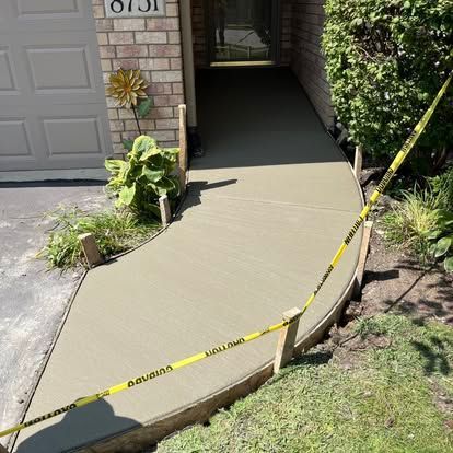 New concrete walkway, curved, leading to house entrance. Yellow caution tape surrounds the fresh cement.