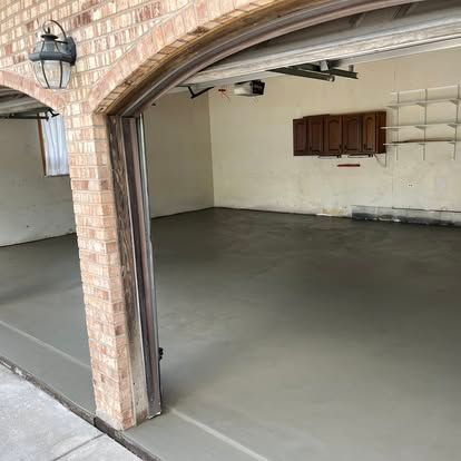 Gray concrete floor inside a garage with brick archway and cabinets on the wall.