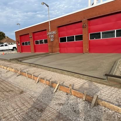 Fire station with red doors, gray concrete, and gravel with wooden framing.
