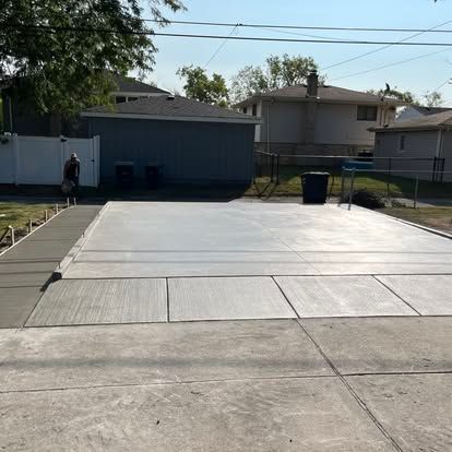 Newly poured concrete patio and walkway in a backyard, with a person nearby and surrounding houses. Newly poured concrete patio and walkway in a backyard, with a person nearby and surrounding houses.