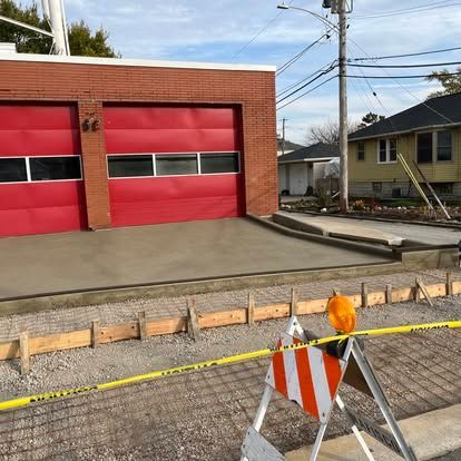 Fire station with red doors, fresh concrete ramp under construction, caution tape and barricades.