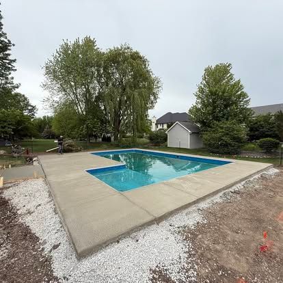 Concrete pool deck surrounding a rectangular pool filled with blue water; construction site.