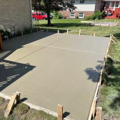 Freshly poured concrete patio with wooden framing in a backyard.