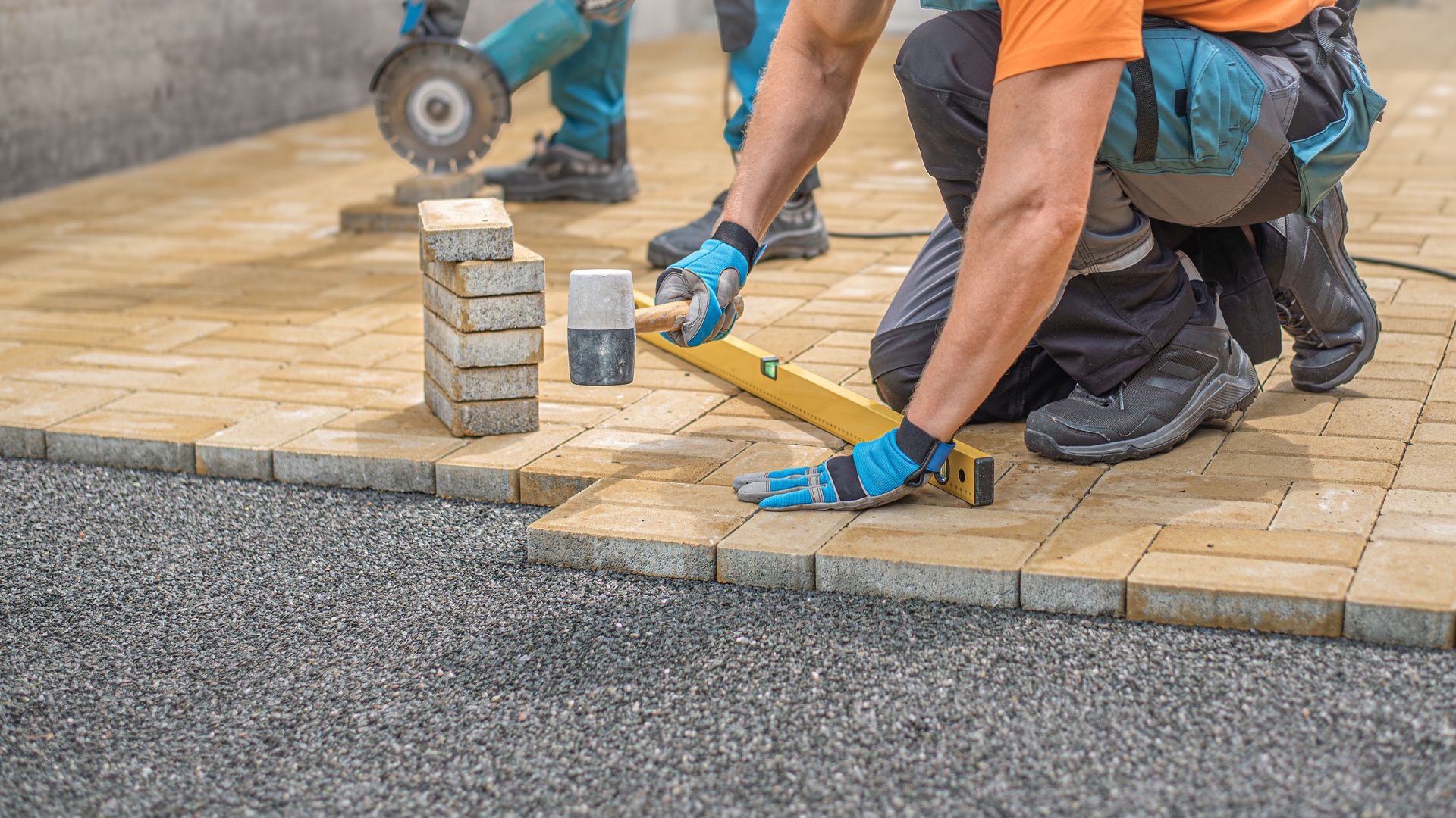 Concrete driveway installation crew leveling paving stones for residential outdoor surface.